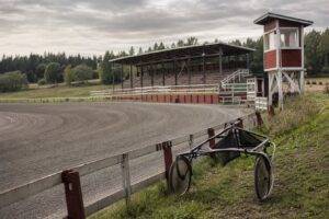 Liten travbana på landsbygden med läktare, domartorn och en sulky vid staketet
