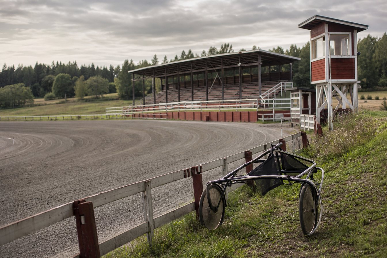 Liten travbana på landsbygden med läktare, domartorn och en sulky vid staketet